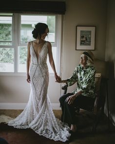 a woman in a wedding dress holding the hand of a man who is sitting on a chair