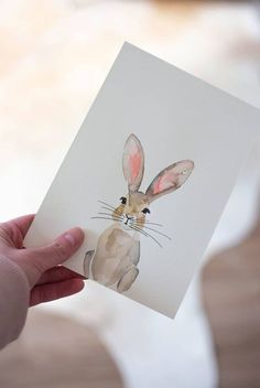 a person holding up a card with a painting of a rabbit on it's face