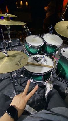 a person's hand is pointing at the green drum set