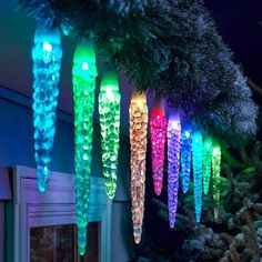 colorful lights hanging from a christmas tree in the dark, with snow on the ground