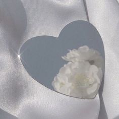 a heart shaped box with white flowers in it sitting on a satin material background,