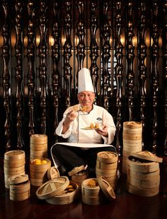 a chef is sitting on the floor surrounded by stacks of bamboo baskets and oranges