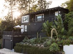 there is a black house with plants in the front yard and trees on the other side