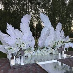 an arrangement of white feathers and flowers on a table in the middle of a park