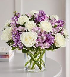 a vase filled with white and purple flowers on top of a table next to a book