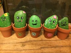 five green cactuses with faces painted on them in clay pots sitting on a wooden table