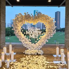 a heart - shaped arrangement with candles and flowers in front of a cityscape