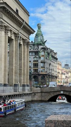 a boat traveling down a river next to tall buildings with statues on the top of them