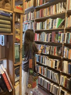 a person standing in front of a bookshelf filled with lots of books and holding a bag