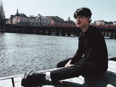 a young man sitting on top of a wooden pier