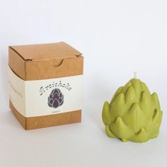 an artichoke is next to a box on a white surface with a small candle in it