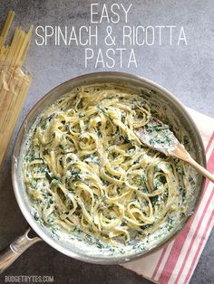 a pan filled with pasta and spinach on top of a towel next to two wooden utensils