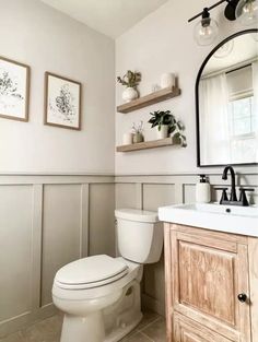 a white toilet sitting next to a sink in a bathroom under two framed pictures on the wall