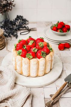 a cake with strawberries on top is sitting on a table next to other plates and utensils