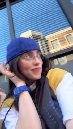 a woman with glasses and a blue hat is talking on her cell phone while standing in front of a building