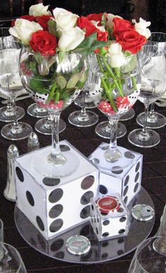 a table topped with wine glasses filled with roses and dices on top of each other