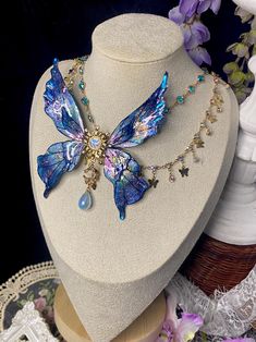 Enchant your look with this stunning handcrafted fairy wing necklace, a magical piece that brings the ethereal beauty of fantasy to life. ️ Design Features: - Centerpiece: Large, intricately detailed fairy/butterfly wings - Wings Color: Mesmerizing blend of iridescent blue and purple - Material: High-quality resin with a glossy, multidimensional finish - Chain: Delicate gold-toned chain with assorted charms ✨ Unique Elements: - Central sun/flower motif connecting the wings - Dangling opalescent Blue Fairy Jewelry For Party, Blue Fairy-style Jewelry For Party, Iridescent Fairy Jewelry For Parties, Iridescent Fairy-style Jewelry For Parties, Handmade Blue Fairycore Jewelry, Iridescent Fairy Style Jewelry For Party, Handmade Iridescent Fantasy Jewelry, Handmade Butterfly Necklaces In Fairycore Style, Handmade Butterfly Fairycore Necklaces