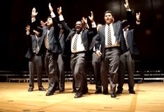 a group of men in suits and ties standing on a stage with their hands up