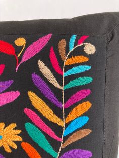 a black pillow with multicolored embroidered leaves on it's back and sides