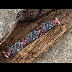 a beaded bracelet sitting on top of a piece of wood next to a rock