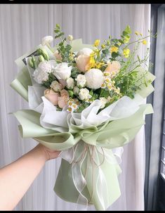 a bouquet of flowers is being held by someone's hand in front of a window