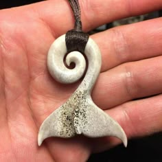 a hand holding a white and brown pendant with a spiral design on it's side