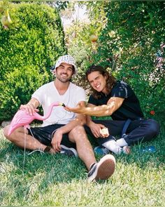 a man and woman sitting on the grass with a pink flamingo in their hand