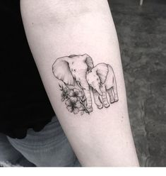 an elephant and baby elephant tattoo on the left arm, with flowers in front of them