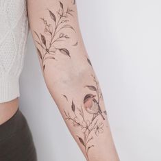 a woman's arm with a bird and flowers tattoo on the left side of her arm