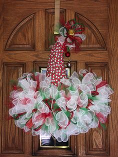 a wreath is hanging on the front door with red, green and white mesh flowers