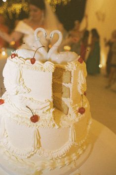 a wedding cake with swans on top and cherries around the edges is sitting on a table