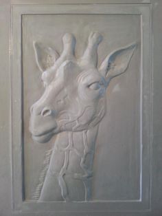 a giraffe is carved into the side of a white wall with a frame