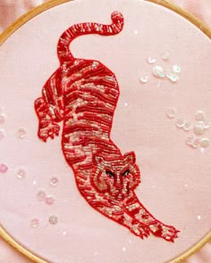 a red tiger embroidered onto a pink fabric with sequins on the bottom and in the middle