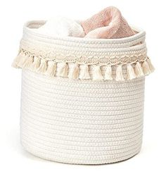 a white basket with tassels and a pink blanket in it on a white background