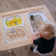 a toddler is playing with his toys on the wooden table in front of him