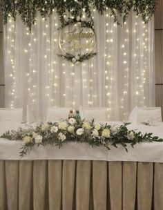 a table with white flowers and greenery on it in front of a curtained wall