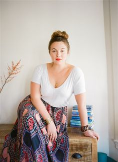 a woman sitting on top of a table next to a stack of books and a plant