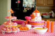 a pink and white table topped with lots of food next to a cake on top of a plate