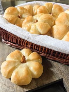 bread rolls in a wicker basket on a wooden table next to a loaf of bread