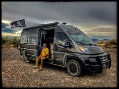 a man sitting in the doorway of a van with a pirate flag on it's roof