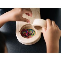 a child is playing with wooden rings in a bowl on the table next to another child's hand