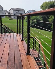 a wooden deck with black railing and handrails in front of houses on a green lawn