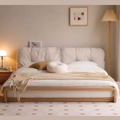 a white bed sitting in a bedroom next to a lamp on a table and a window