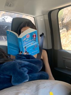 a woman sitting in the back seat of a car reading a book