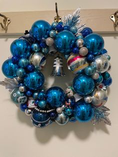 a christmas wreath hanging on the wall with ornaments in blue and silver colors around it