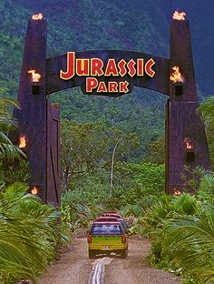 a car driving down a dirt road under a sign that says jurastic park