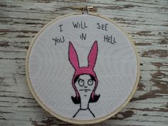 a cross - stitch hoop hanging on a wooden surface with a drawing of a woman wearing pink bunny ears