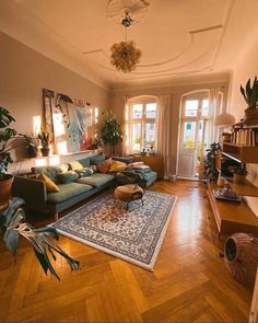 a living room filled with lots of furniture and plants on top of a hard wood floor