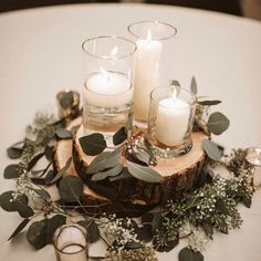 candles and greenery are arranged on a wood slice