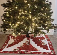 a small christmas tree with white lights on it and a red blanket under the tree